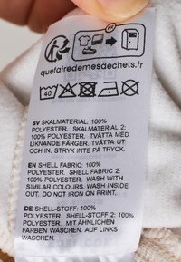 Etichetta di cura in tessuto bianco con testo nero, che dettagli le istruzioni di lavaggio e la composizione del materiale: 100% poliestere, include sezioni multilingue.