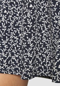 Laivastonsininen kangas valkoisella kukkakuviolla, jossa on herkkiä lehtiä ja nuppuja. Pinta on sileä, virtaava kuosi ja suora helma.