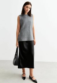 Grå ärmlös stickad topp som matchas med en svart satin midi-kjol och svarta spetsiga ballerinat. Accessoarer med en svart handväska.
