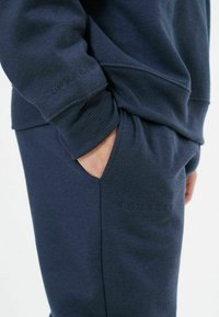 Dunkelblaues Sweatshirt- und Hosen-Set, hergestellt aus weichem Baumwollmix. Verfügt über gerippte Bündchen und dezente Markenkennung am Ärmel und Taschenbereich.