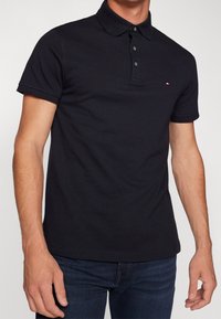 Marinblå polo t-shirt med krage, korta ärmar, treknappslås och broderad logotyp på vänster bröst. Slät tygkvalitet.