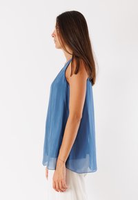 Top senza maniche in chiffon blu con una vestibilità morbida, leggero lucido e orlo arrotondato, visto di lato, caratterizzato da una delicata texture e caduta.