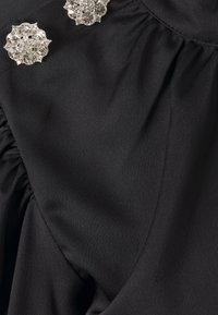 Tissu noir plissé avec deux broches argentées décoratives ornées de plusieurs pierres précieuses claires au niveau de l'épaule.