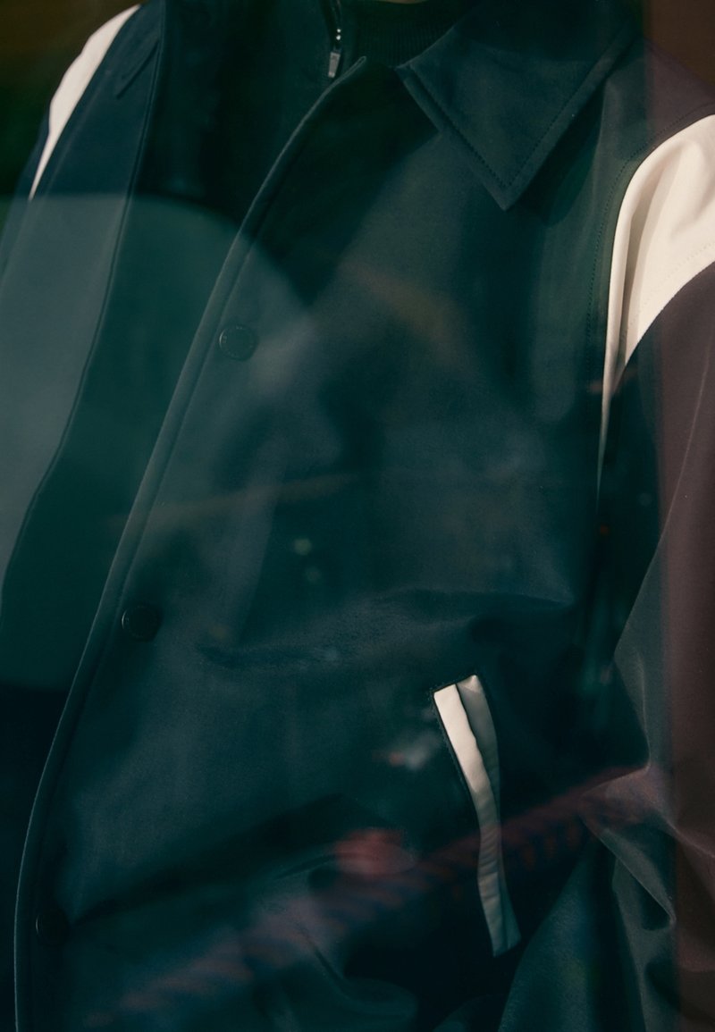 Kurtka w czarno-białe płaty z zamkiem błyskawicznym, ozdobami z guzików i boczną kieszenią. Gładka tekstura o nowoczesnym designie.