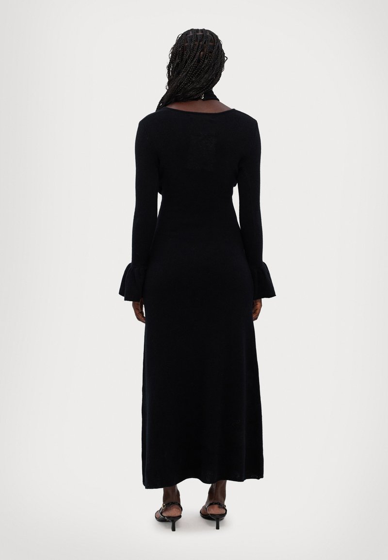 Abito maxi nero a maniche lunghe con corpino aderente, polsini a campana e una texture liscia. La schiena presenta un design aperto. Stile semplice ed elegante.