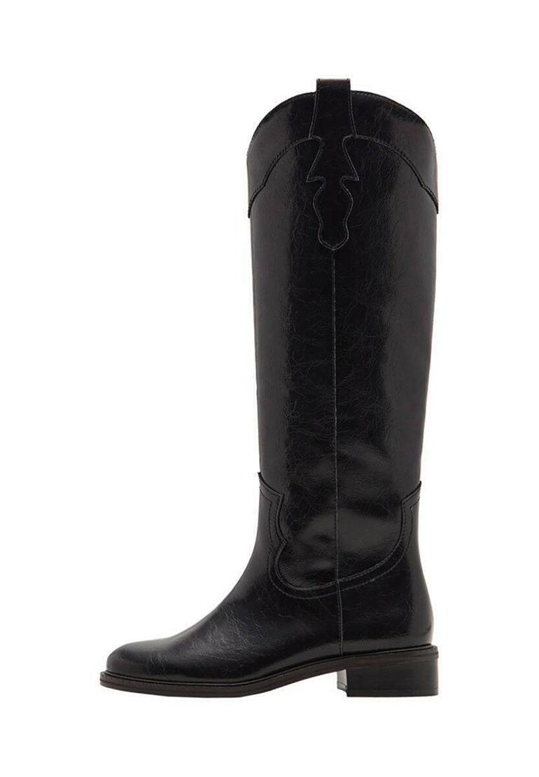 Bota de cuero negra hasta la rodilla con un acabado texturizado, que presenta un diseño recortado en la parte superior y un tacón bajo apilado. Superficie lisa con costuras decorativas.