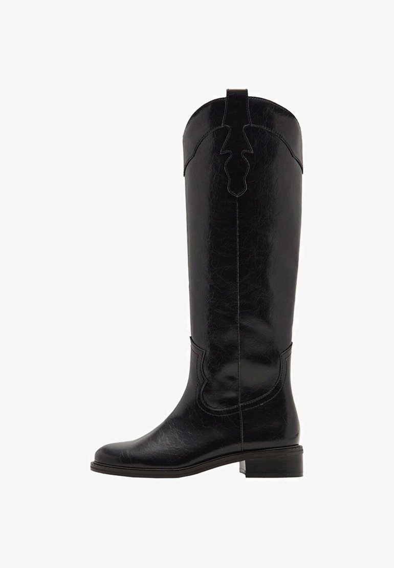 Bota de cuero negra hasta la rodilla con un acabado texturizado, que presenta un diseño recortado en la parte superior y un tacón bajo apilado. Superficie lisa con costuras decorativas.