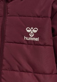 Burgundy puffer jacket with quilted texture, featuring a white embroidered logo on the chest and a front zipper closure.