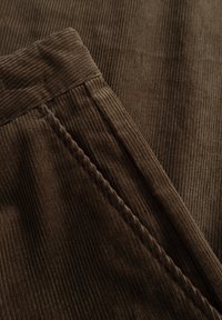 Bruin corduroy stof met verticale ribbels heeft een gladde tailleband en subtiele stiksels langs de naden.