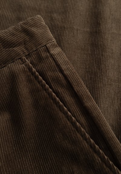 Tissu en velours côtelé brun avec des côtes verticales, dotée d'une taille lisse et de détails de couture subtils le long des coutures.
