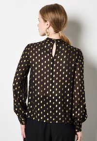 Schwarze Bluse mit goldenen Punkten, langen Ärmeln und Rückenausschnitt, aus leichtem Stoff mit glatter Textur.