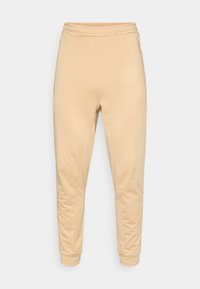 Bézs színű melegítőnadrág elasztikus derékpánttal, szűkülő mandzsettákkal és oldalzsebekkel. Az anyag sima, enyhén nyújtható.