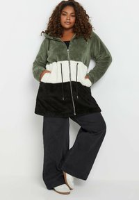 Huvtröja i fleece med färgblockdesign i olivgrön, krämfärgad och svart, med dragkedja fram och justerbar dragsko i midjan.