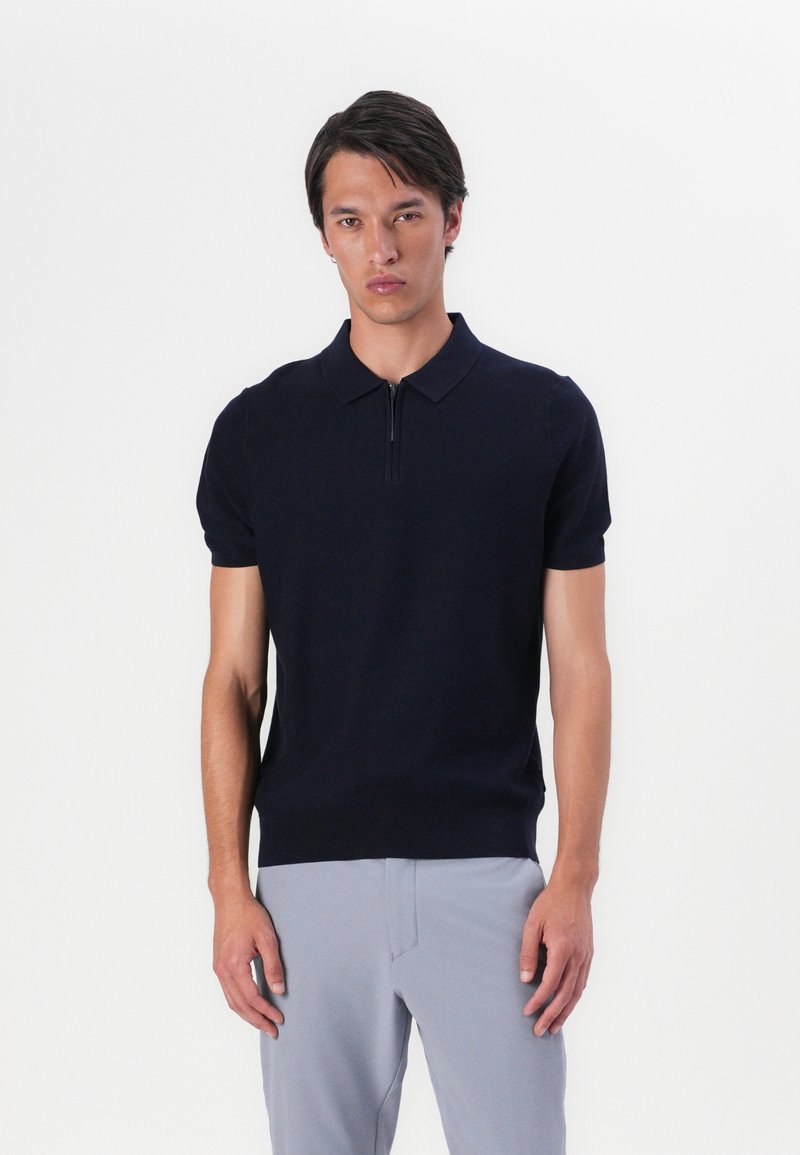 Marineblå kortermet polo skjorte med halv-zip krage. Laget av glatt stoff, tettsittende design, og med ribbestrikket kant for et strukturert utseende.
