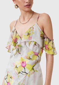 Bloemrijke jurk van doorschijnende stof, met cold shoulder ontwerp, ruches bij de halslijn en een levendig patroon van gele en roze orchideeën.