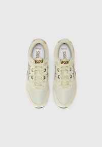 Baskets de sport beiges avec un design en mesh et en suède, dotées d'une semelle blanche et d'accents noirs. Les lacets sont également beiges, avec une semelle intérieure de marque.