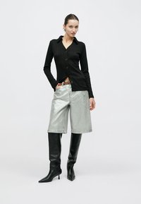 Μαύρο ριμπ κοντομάνικο πουκάμισο με κουμπιά, ασημένια μεταλλικά σορτς μήκους μέχρι το γόνατο και μαύρες μπότες μέχρι το γόνατο με μυτερή μύτη. Απλός σχεδιασμός με αντιθετικές υφές.