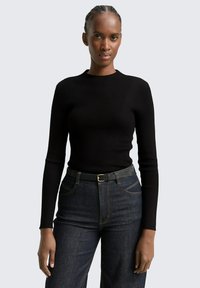 Schwarzes, geripptes Langarmoberteil mit Rundhalsauschnitt, kombiniert mit dunkelblauen, hoch taillierten Jeans und einem schlanken schwarzen Gürtel mit einer goldenen Schnalle.