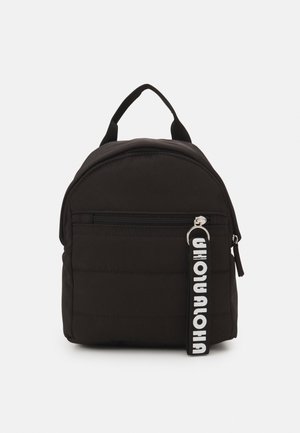 Sac à dos rembourré noir de forme ronde, avec une poche frontale zippée et un tissu ton sur ton. Possède une étiquette de marque bien visible en blanc sur la tirette du zip.