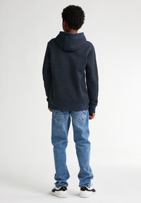 Felpa navy con tessuto testurizzato, cucitura sulla spalla posteriore, tasca a marsupio; abbinata a jeans in denim chiaro con tasche posteriori e cuciture sottili.