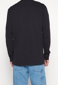 Černé tričko s dlouhým rukávem z bavlny, s kulatým výstřihem a rovný lemem. Tkanina vypadá hladká bez viditelných vzorů.