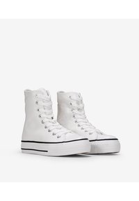 Zapatillas de lona altas blancas con ojetes plateados, ribete de suela de goma negra y un acabado texturizado en la parte superior. Diseño clásico de cordones.
