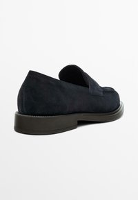 Zwarte suède instapschoenen met een afgeronde neus, minimalistisch ontwerp en een stevige rubberen zool met subtiele stikaccenten.