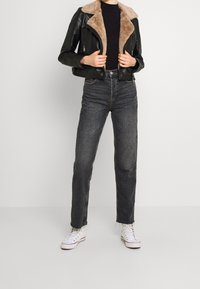 Zwarte leren cropped jas met een beige faux fur kraag, gecombineerd met high-waisted donkergrijze jeans en witte sneakers.