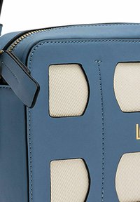 Sac en cuir bleu avec des découpes en tissu beige, présentant une forme rectangulaire, un marquage doré et une quincaillerie de fermeture éclair noire.