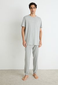 Grijze katoenen pyjama set bestaande uit een T-shirt met korte mouwen en een ronde hals, en een broek met elastische manchetten. Subtiele logo-detail op het shirt.