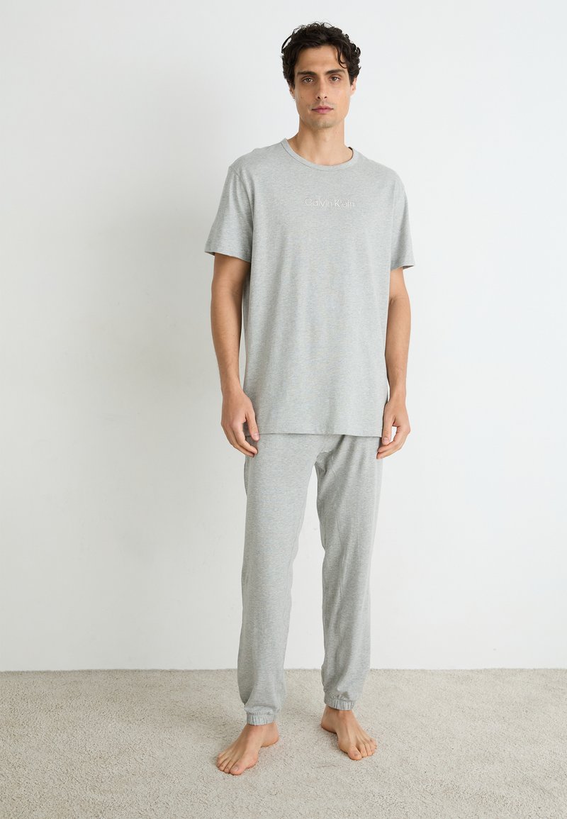 Grijze katoenen pyjama set bestaande uit een T-shirt met korte mouwen en een ronde hals, en een broek met elastische manchetten. Subtiele logo-detail op het shirt.