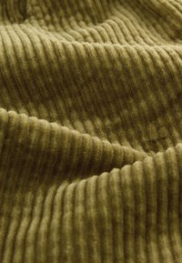 Getextureerde groene corduroy stof met verticale ribbels, met een zachte, harige oppervlakte en rijke kleurvariatie.