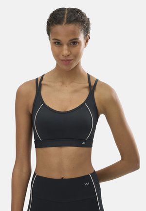 Mujer con trenza que lleva un top deportivo negro y leggings de talle alto a juego con detalles de costuras blancas.