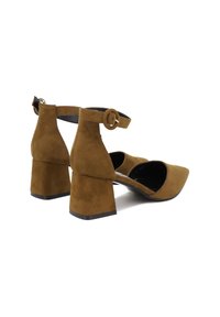 Scarpe in suede marrone con tacco a blocco, cinturino alla caviglia e fibbia rotonda. Punta appuntita e lati con ritagli per un tocco di dettaglio in più. Fodera interna nera.