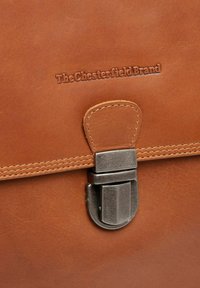 Bruine leren tas met een metalen sluiting en gestikte accenten. Voorzien van reliëfbranding en een gladde, matte textuur.