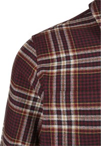 Rutet skjorte i burgunder, svart og hvit med gule detaljer. Har en vevd tekstur og et distinkt rutemønster på stoffet.