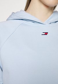 Jasnoniebieska bluza z kapturem o miękkiej fakturze. Posiada małe, haftowane logo w granatowym, czerwonym i białym kolorze na klatce piersiowej. Podwójnie wyłożony kaptur.