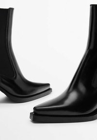 Black ankle boots made of shiny material with a pointed toe and a flat sole. Features elastic side panels and a sleek design.