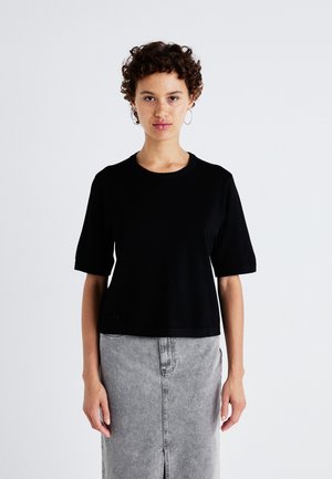 Schwarzes kurzärmliges Crop-Top aus weichem Stoff mit Rundhalsausschnitt. Kombiniert mit einem hellgrauen Jeansrock mit einem Schlitz vorne.
