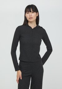 Felpa nera con zip e righe, dal design aderente e con maniche lunghe. Presenta un cappuccio e una sottile texture su tutto il tessuto.