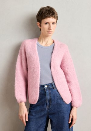 Pink fluffy cardigan with a loose fit, round neck, and long sleeves, layered over a light blue T-shirt, paired with high-waisted denim jeans.