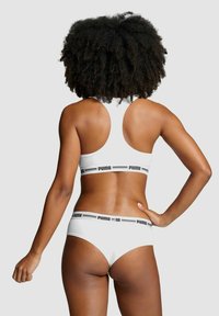 White sports bra and matching underwear feature a snug fit with black "PUMA" logo bands. The fabric appears smooth with minimal seams.