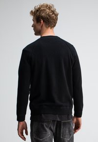Schwarzer Pullover mit langen Ärmeln und gerippten Bündchen. Weicher Stoff, Rundhalsausschnitt und schlichte Rückseite, kombiniert mit grauen Jeans.