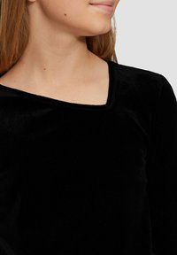 Schwarzes Samtoberteil mit Rundhalsausschnitt und langen Ärmeln, das eine weiche Textur und ein figurbetontes Design aufweist. Nahaufnahme des oberen Oberkörpers.