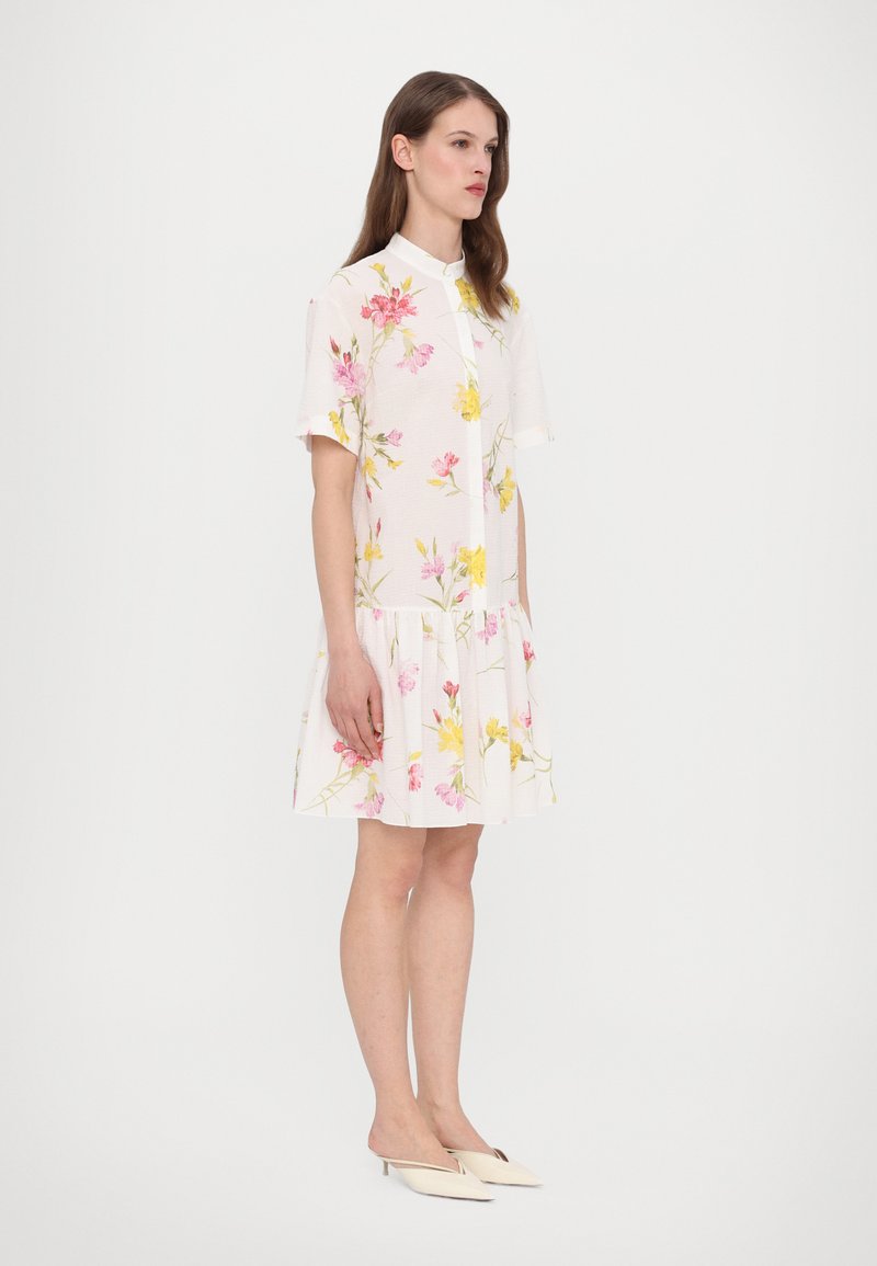 Robe florale blanche à manches courtes, ornée de motifs de fleurs roses et jaunes et d'une ourlet évasé. Texture de tissu lisse.