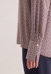 Camicia button-up con un motivo geometrico bordeaux e crema. Maniche lunghe con polsini abbottonati, il tessuto appare leggero e morbido.