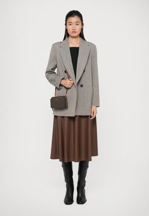 Grå dobbelspent blazer over en svart topp, brun plissert skjørt og svarte kne høye støvler. Brun crossover-veske med mønsterdetaljer.