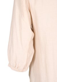 Blusa beige chiaro con maniche lunghe a sbuffo, polsini con bottoni e un tessuto testurizzato che aggiunge una sottile dimensione.