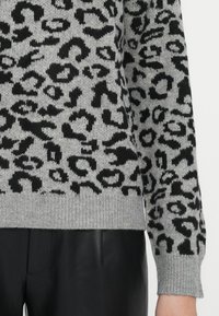 Pull en tricot gris avec un motif léopard noir, poignets et ourlet côtelés, associé à un pantalon en cuir noir.