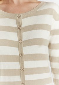 Beige-weißer gestreifter Cardigan mit rundem Ausschnitt und fünf runden Knöpfen vorne. Weicher Strickstoff mit gerippten Kanten.